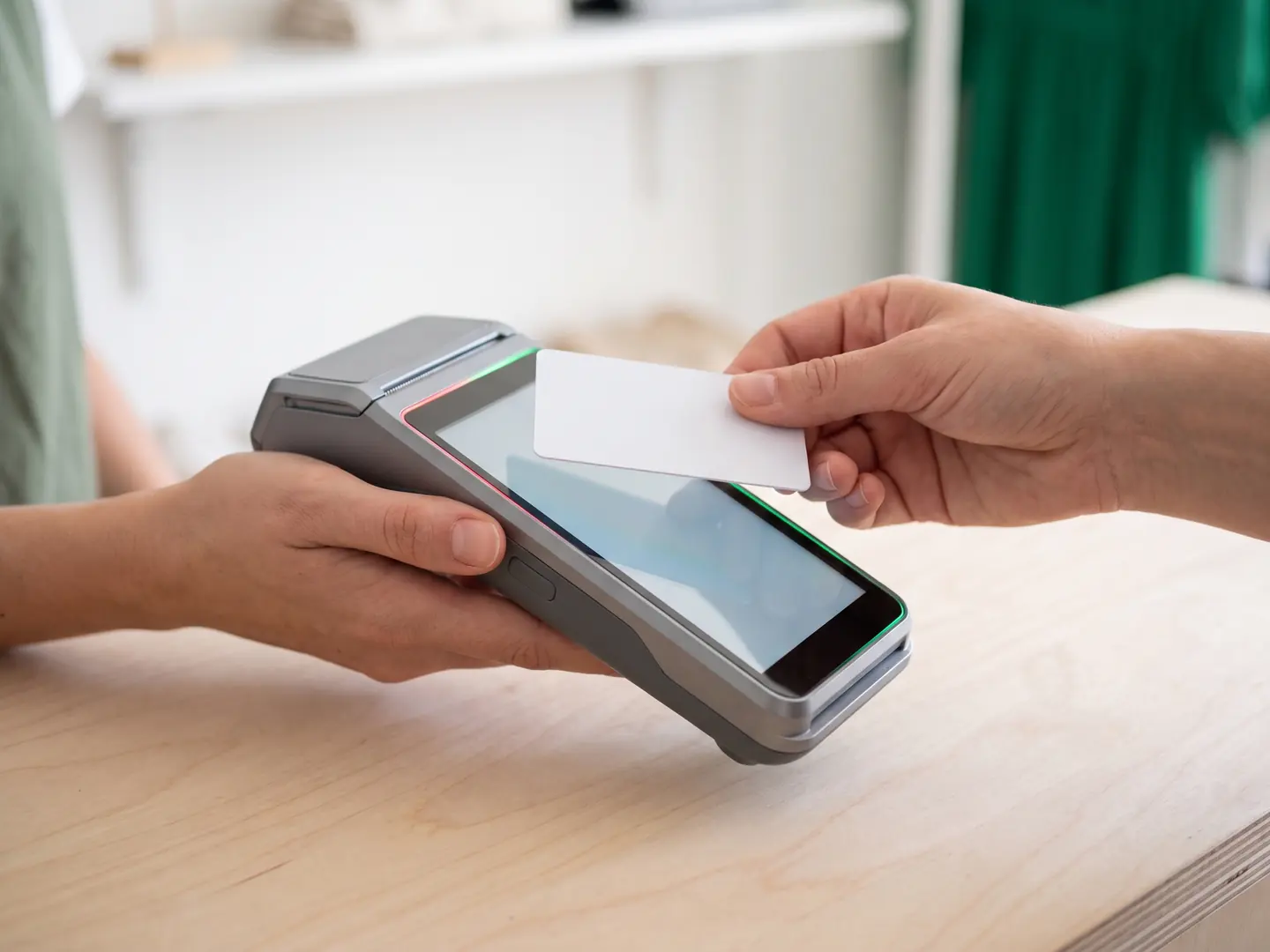 A customer tapping a card on a modern smart POS terminal at a shop counter